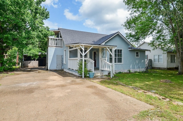 view of front facade with a porch, a shingled roof, a front yard, and driveway