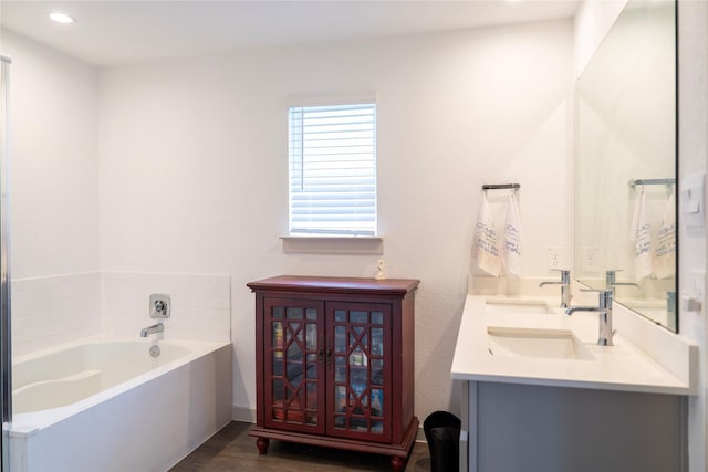 bathroom featuring recessed lighting, wood finished floors, double vanity, a bath, and a sink