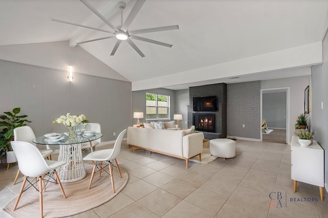 living area with light tile patterned flooring, a brick fireplace, a ceiling fan, and lofted ceiling with beams