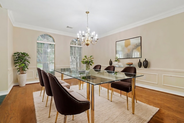 dining room with a chandelier, crown molding, visible vents, wainscoting, and wood finished floors