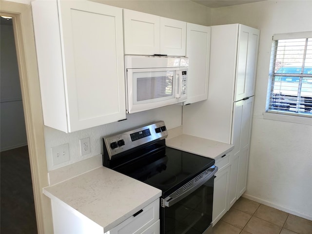 kitchen featuring light tile patterned floors, white cabinetry, baseboards, range with electric stovetop, and white microwave