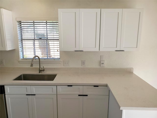 kitchen with stainless steel dishwasher, white cabinetry, light countertops, and a sink