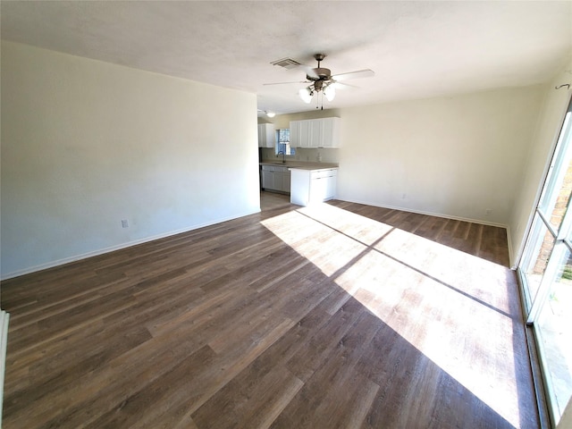 unfurnished living room with baseboards, a sink, dark wood-style floors, visible vents, and a ceiling fan