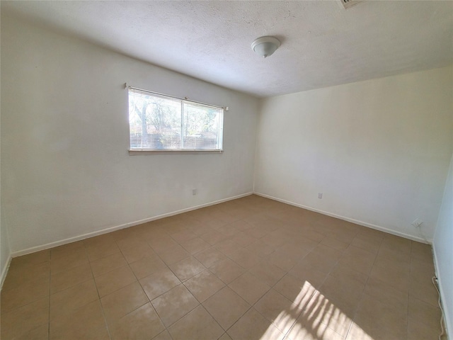tiled empty room with a textured ceiling and baseboards