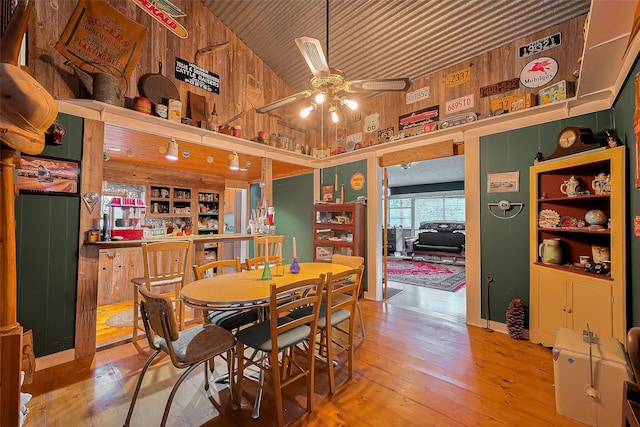 dining space with a ceiling fan, a towering ceiling, wood walls, wooden ceiling, and wood-type flooring