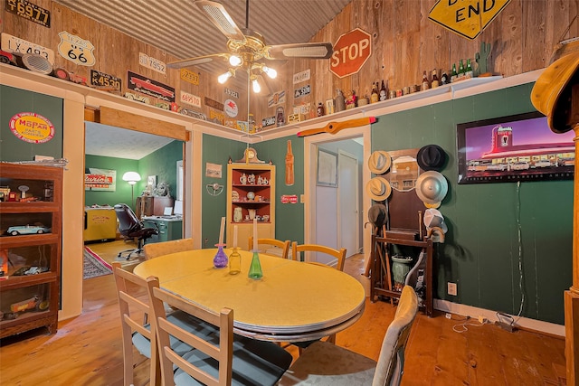 dining room featuring a ceiling fan, a towering ceiling, wood finished floors, and wood walls