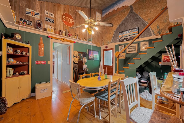 dining space with wood-type flooring, ceiling fan, a high ceiling, and stairway