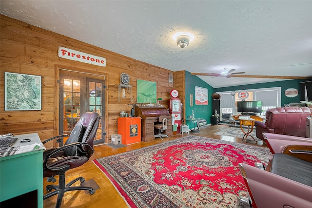 living room with ceiling fan, a textured ceiling, wood walls, wood finished floors, and vaulted ceiling