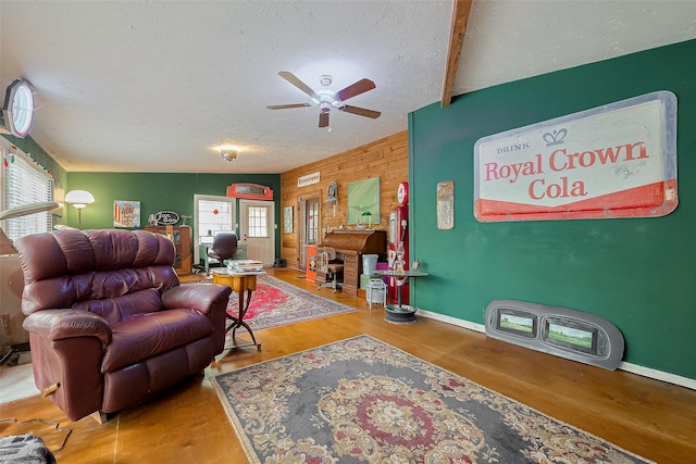 living area with wood walls, a textured ceiling, a ceiling fan, and wood finished floors