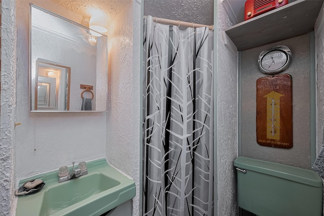 bathroom featuring a sink, a textured wall, a shower with shower curtain, and toilet