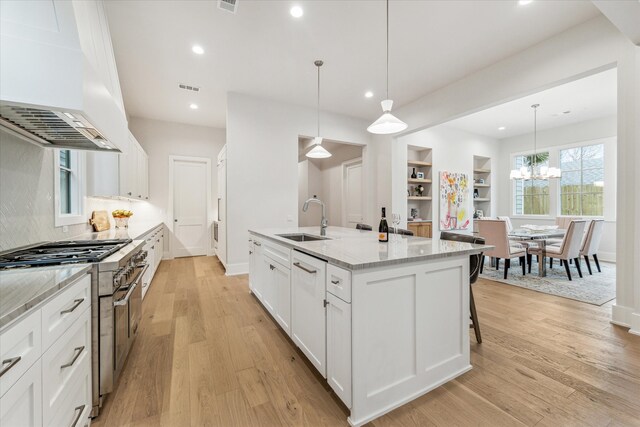 714 E 21st St, Houston, TX 77008 - kitchen featuring an island with sink, light wood-style flooring, stainless steel stove, a sink, and white cabinetry