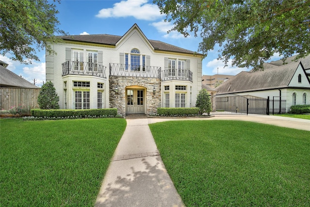 view of front facade featuring a front lawn, a balcony, stone siding, french doors, and a gate