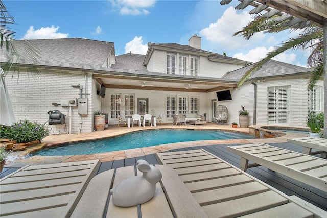 back of property with brick siding, an in ground hot tub, an outdoor pool, and a chimney