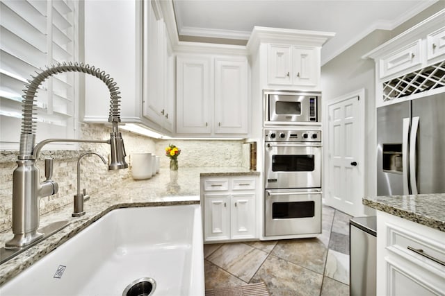 kitchen with white cabinets, crown molding, appliances with stainless steel finishes, a sink, and backsplash