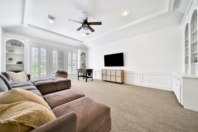 living room featuring a ceiling fan, visible vents, light colored carpet, built in shelves, and a tray ceiling