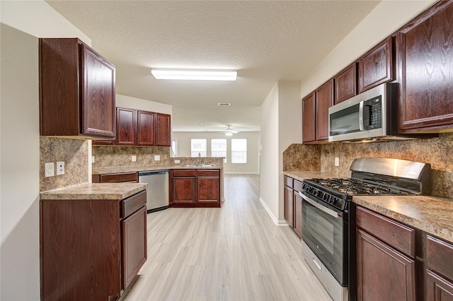 kitchen with ceiling fan, a sink, decorative backsplash, light wood-style floors, and appliances with stainless steel finishes