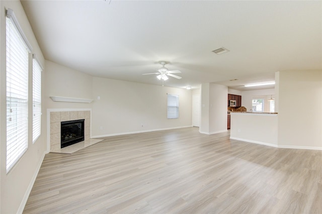 unfurnished living room featuring a ceiling fan, baseboards, a tiled fireplace, and light wood-type flooring