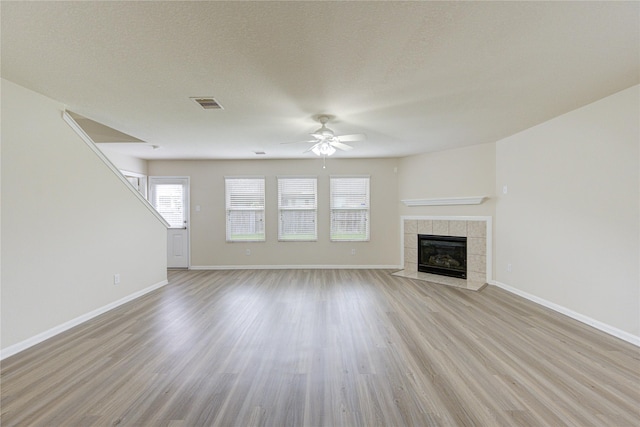 unfurnished living room featuring a tiled fireplace, light wood-type flooring, visible vents, and a ceiling fan