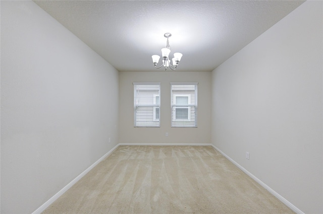 spare room featuring light colored carpet, an inviting chandelier, and baseboards