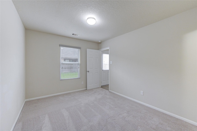 empty room featuring a textured ceiling, light carpet, baseboards, and visible vents