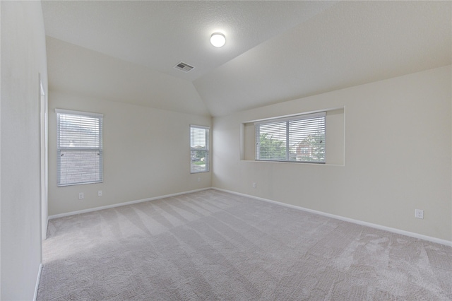 spare room with baseboards, light carpet, visible vents, and lofted ceiling