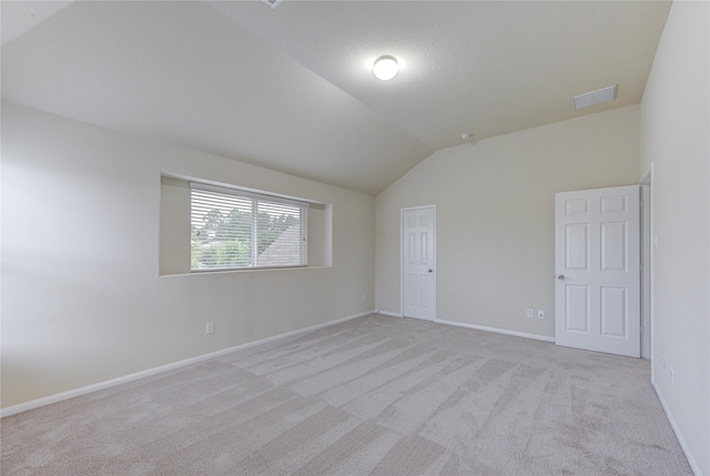 spare room featuring light colored carpet, visible vents, baseboards, and lofted ceiling