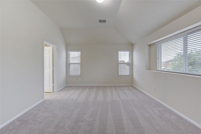 spare room with vaulted ceiling, light colored carpet, baseboards, and visible vents