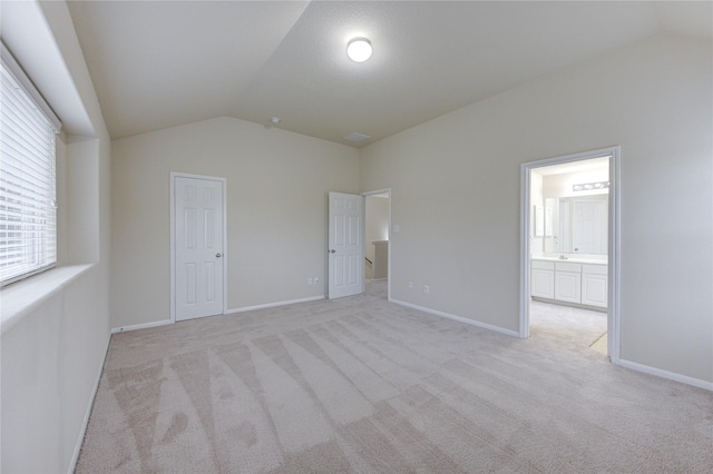 unfurnished bedroom with lofted ceiling, light carpet, connected bathroom, and baseboards