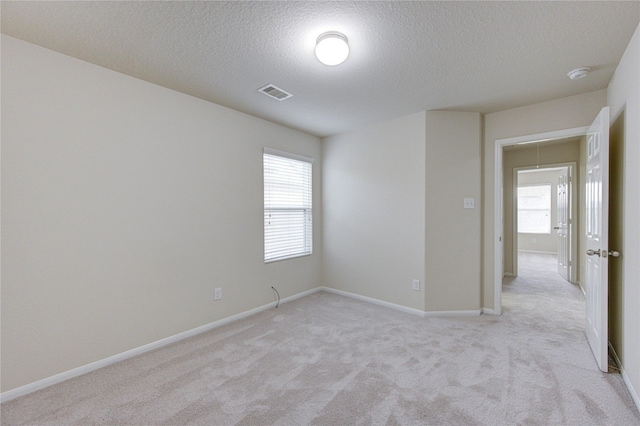 spare room featuring baseboards, light carpet, visible vents, and a textured ceiling
