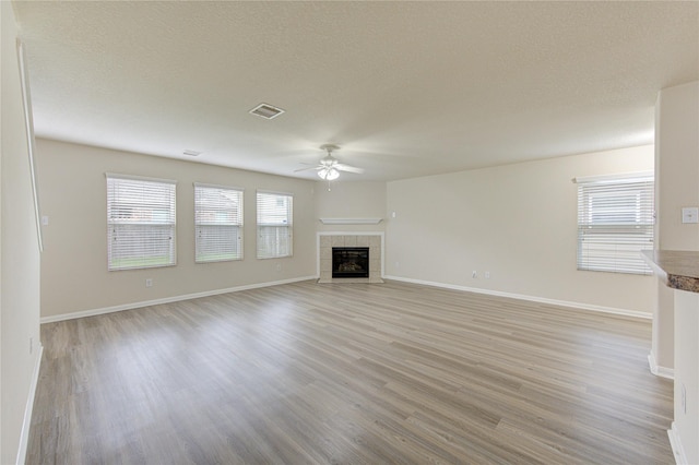 unfurnished living room with light wood-style flooring, a ceiling fan, a fireplace, visible vents, and baseboards
