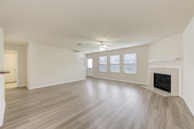 unfurnished living room with a ceiling fan, baseboards, light wood finished floors, and a tiled fireplace