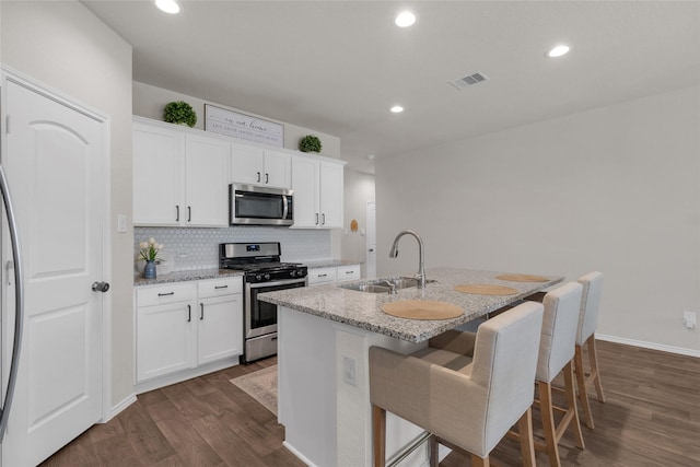 kitchen featuring decorative backsplash, visible vents, appliances with stainless steel finishes, a sink, and dark wood-type flooring