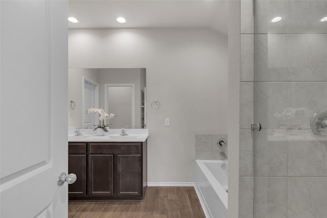 bathroom with a garden tub, double vanity, wood finished floors, baseboards, and a shower with shower door