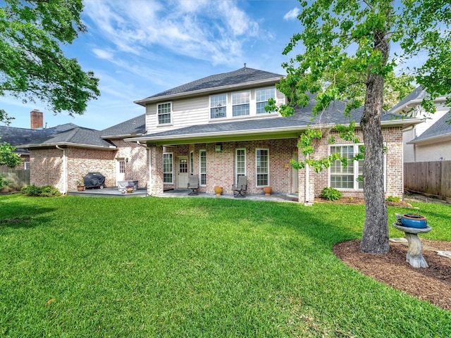 traditional home with a patio area, a shingled roof, fence, a front lawn, and brick siding