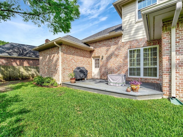 back of property with fence, a wooden deck, a shingled roof, a lawn, and brick siding