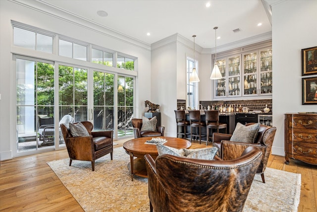 living area with bar area, visible vents, ornamental molding, and light wood-style floors