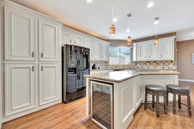 kitchen featuring a kitchen island, backsplash, black fridge with ice dispenser, light wood finished floors, and beverage cooler