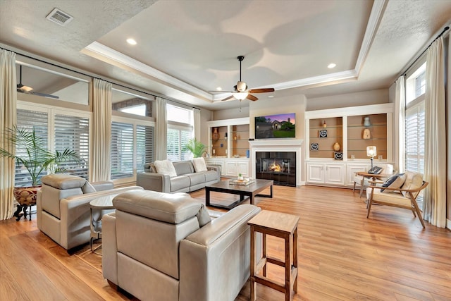 living area with a ceiling fan, a raised ceiling, and light wood finished floors