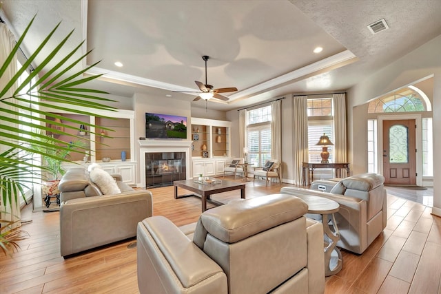 living room with visible vents, light wood-style flooring, a raised ceiling, and a ceiling fan