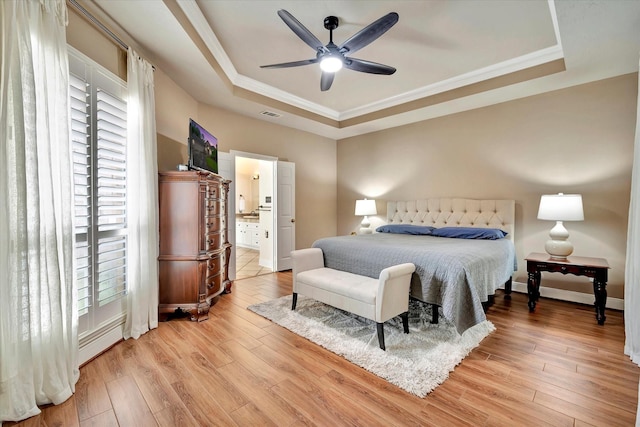 bedroom with visible vents, crown molding, light wood-type flooring, a raised ceiling, and connected bathroom