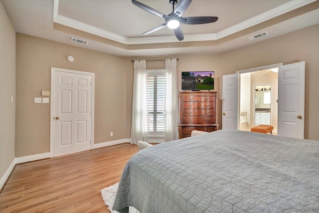 bedroom with a tray ceiling, visible vents, baseboards, and light wood finished floors