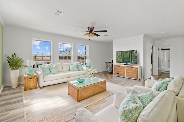living room featuring light wood-style flooring, baseboards, visible vents, a ceiling fan, and crown molding