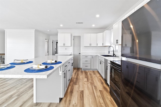 kitchen with light wood-style floors, a kitchen island, a sink, black range with electric stovetop, and crown molding