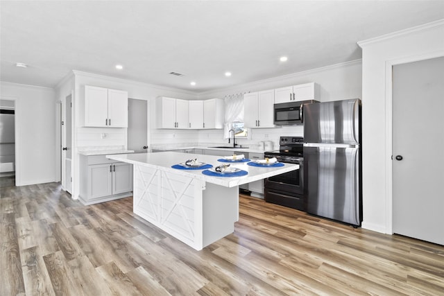 kitchen featuring freestanding refrigerator, black / electric stove, a kitchen island, light countertops, and a sink