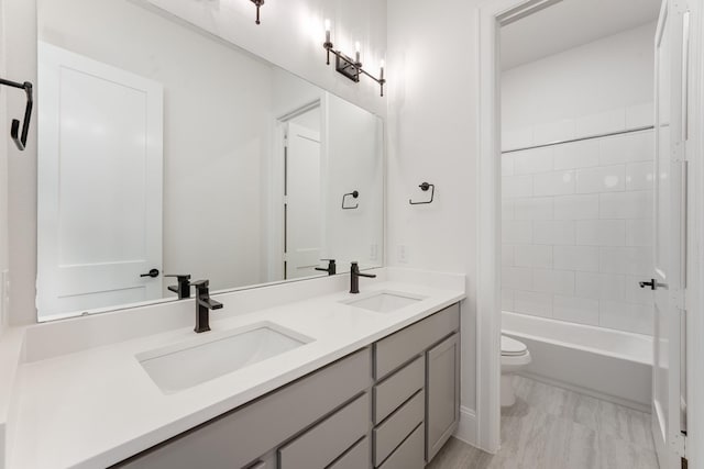 full bath featuring toilet, double vanity, a sink, and shower / bathing tub combination