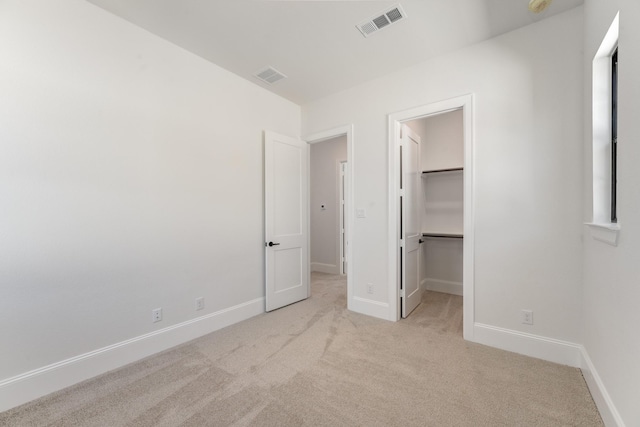 unfurnished bedroom with a walk in closet, visible vents, carpet, and baseboards