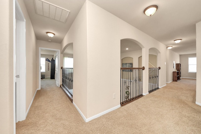 corridor featuring carpet floors, arched walkways, baseboards, and visible vents
