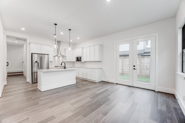 kitchen featuring stainless steel appliances, light countertops, white cabinets, wall chimney exhaust hood, and french doors