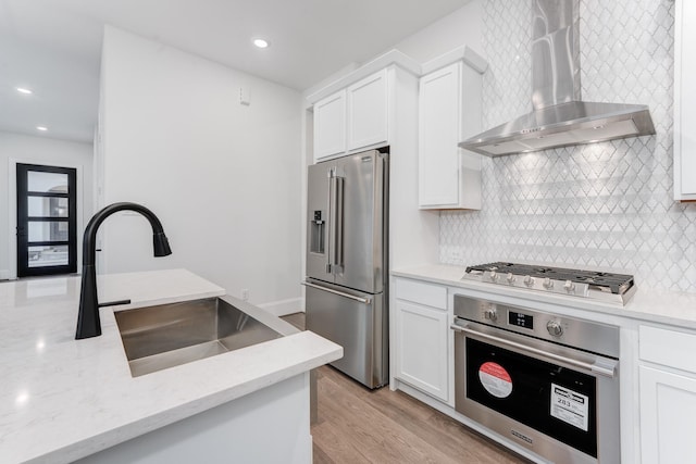 kitchen featuring wall chimney range hood, stainless steel appliances, white cabinets, and a sink