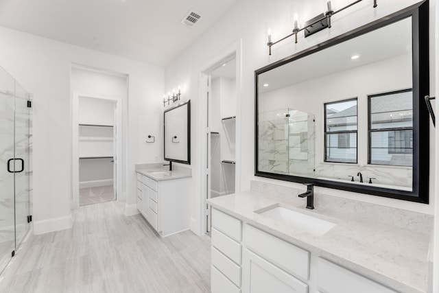 bathroom featuring a spacious closet, two vanities, a sink, visible vents, and a marble finish shower